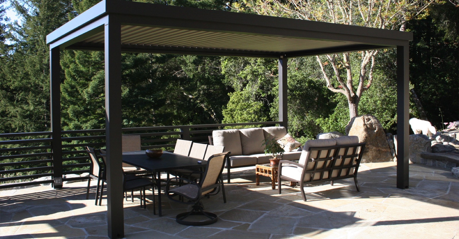 Dark louvered pergola sheltering lounge chairs and a dining table on a flagstone patio